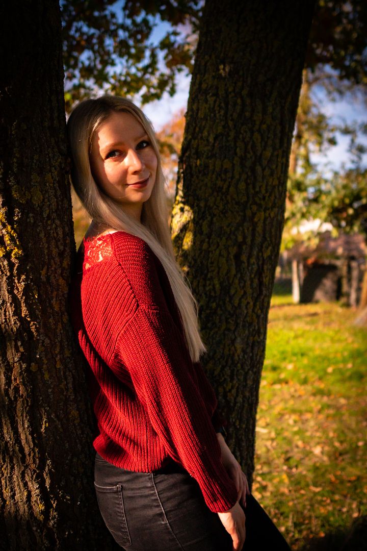 Sophie in einem roten Pullover an einem Baum angelehnt